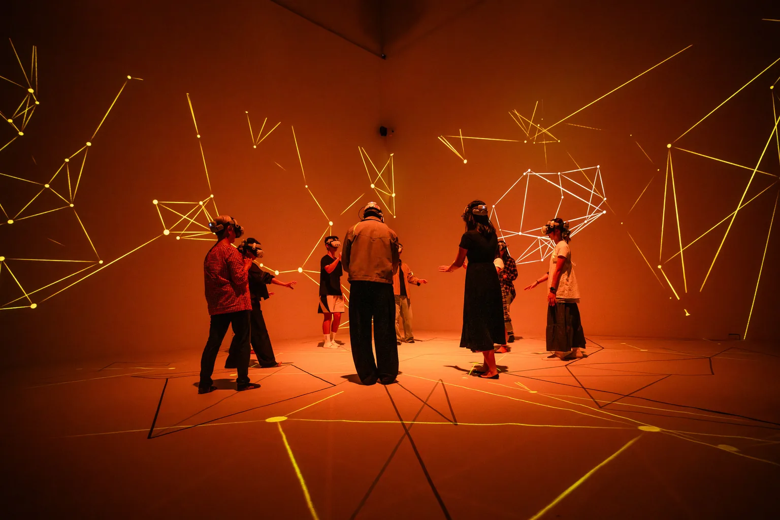 Participants in Shifting Connections wearing VR headsets beneath orange light and projected geometric connections