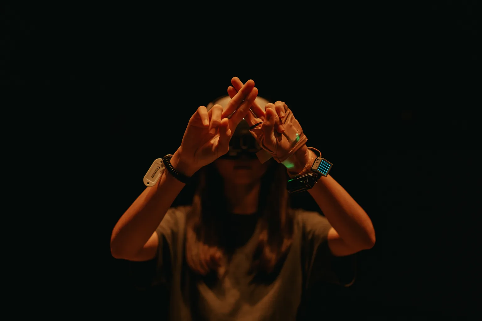 A Beastosis participant wearing a VR headset raises both hands in the dark performance space
